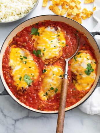 A skillet filled with Salsa Chicken topped with cheese and cilantro with a spoon in it.