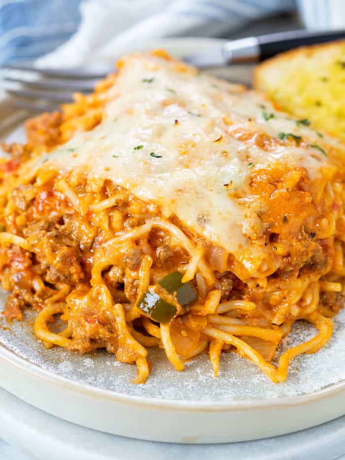 A plate with a slice of baked spaghetti topped with mozzarella cheese and a fork in the background.