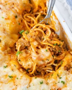 A casserole dish filled with Baked Spaghetti with a spoon scooping it up.