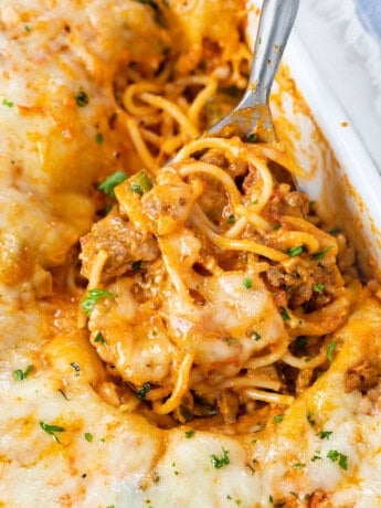 A casserole dish filled with Baked Spaghetti with a spoon scooping it up.