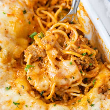 A casserole dish filled with Baked Spaghetti with a spoon scooping it up.