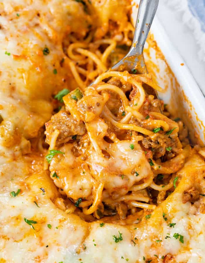 A casserole dish filled with Baked Spaghetti with a spoon scooping it up.
