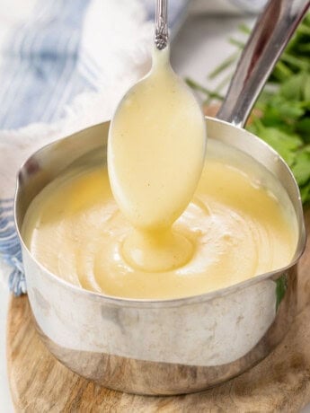 A spoon scooping out homemade Cream of Chicken Soup from a saucepan.