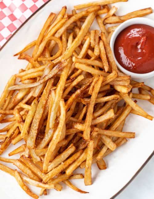 A white platter full of crispy homemade french fries next to a ramekin of ketchup.