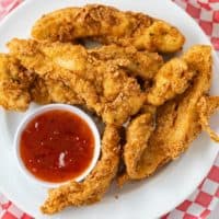 Crispy Fried Chicken Tenders on a white plate with sweet and sour dipping sauce.