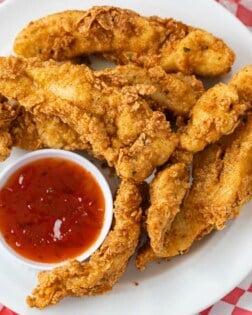 Crispy Fried Chicken Tenders on a white plate with sweet and sour dipping sauce.