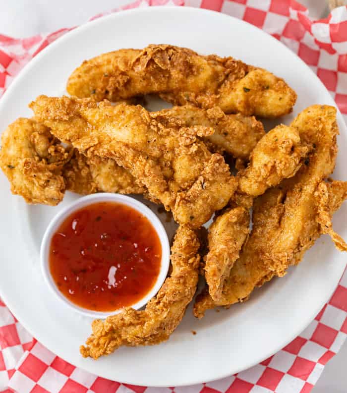 A white plate with fried chicken tenders with sweet and sour sauce.