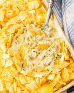 Overhead view of a casserole dish with a spoon in it topped with potato chips and chives.