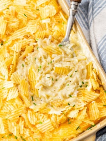 Overhead view of a casserole dish with a spoon in it topped with potato chips and chives.