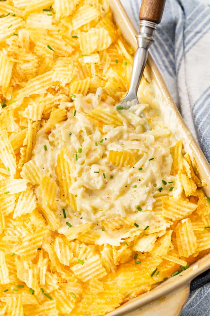 Overhead view of a casserole dish with a spoon in it topped with potato chips and chives.