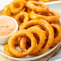 A white plate with crispy beer battered onion rings and dipping sauce.