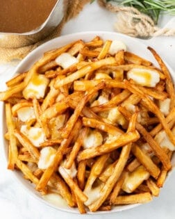 A white plate full of homemade poutine with french fries, gravy, and melted cheese curds.