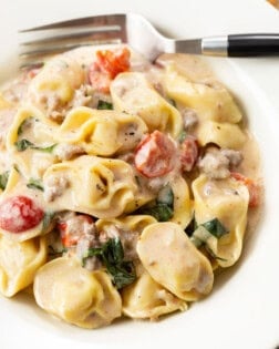 A white bowl filled with tomato basil tortellini pasta in a cream sauce with a fork in the back.