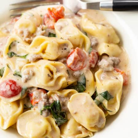 A white bowl filled with tomato basil tortellini pasta in a cream sauce with a fork in the back.