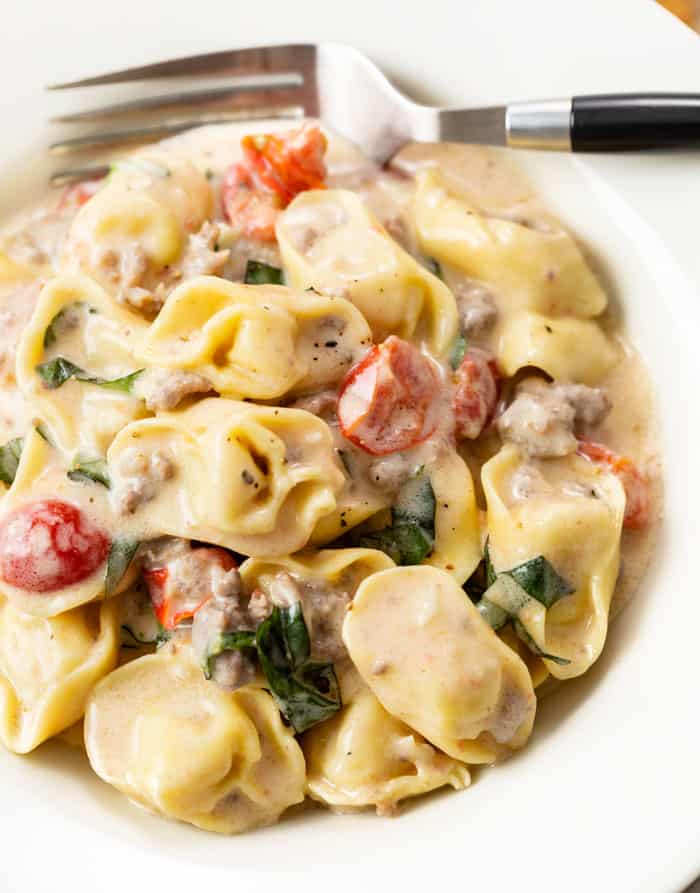 A white bowl filled with tomato basil tortellini pasta in a cream sauce with a fork in the back.