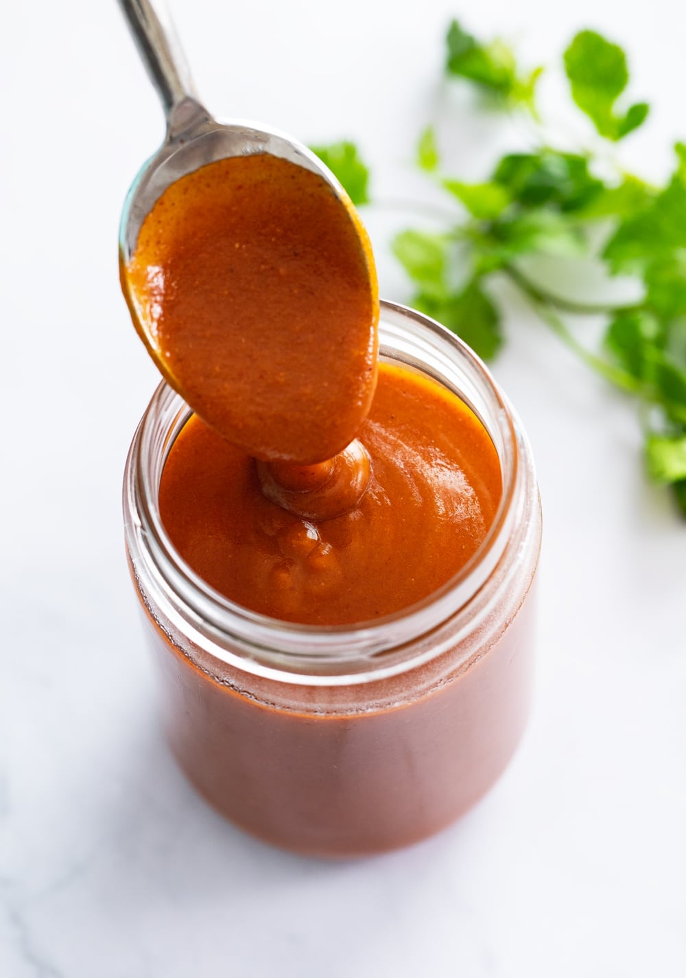 Homemade Enchilada Sauce in a jar with a spoon scooping it out.