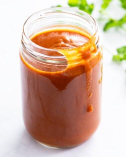 Enchilada Sauce in a jar with fresh cilantro in the background.