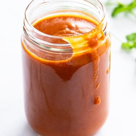Enchilada Sauce in a jar with fresh cilantro in the background.