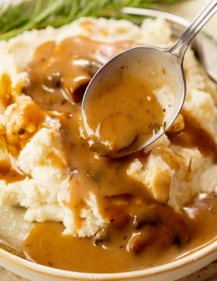 A spoon drizzling mushroom gravy over a pile of mashed potatoes.