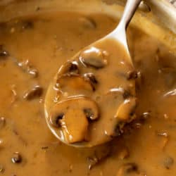 A spoon full of thick and creamy mushroom gravy from a skillet.