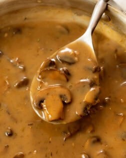 A spoon full of thick and creamy mushroom gravy from a skillet.