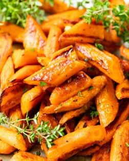 Sliced up roasted carrots piled on top of each other with fresh thyme on the side and in the back.