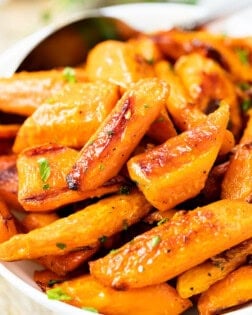 Roasted carrots in a white bowl with a spoon in the background.