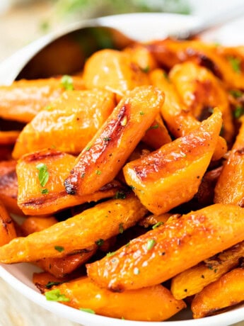 Roasted carrots in a white bowl with a spoon in the background.
