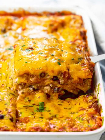 A casserole dish filled with Taco Lasagna that's being pulled up with a spatula.