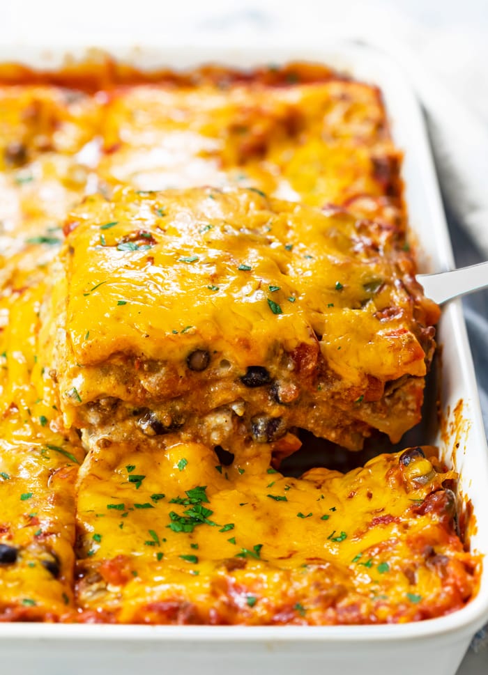 A casserole dish filled with Taco Lasagna that's being pulled up with a spatula.
