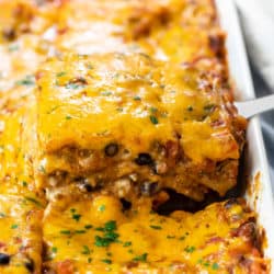 A casserole dish filled with Taco Lasagna that's being pulled up with a spatula.
