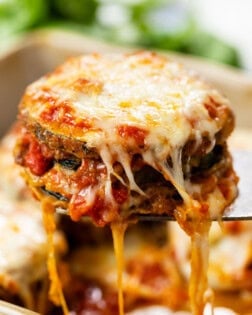 A spatula pulling up cheese zucchini parmesan from a casserole dish.