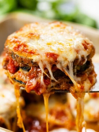 A spatula pulling up cheese zucchini parmesan from a casserole dish.