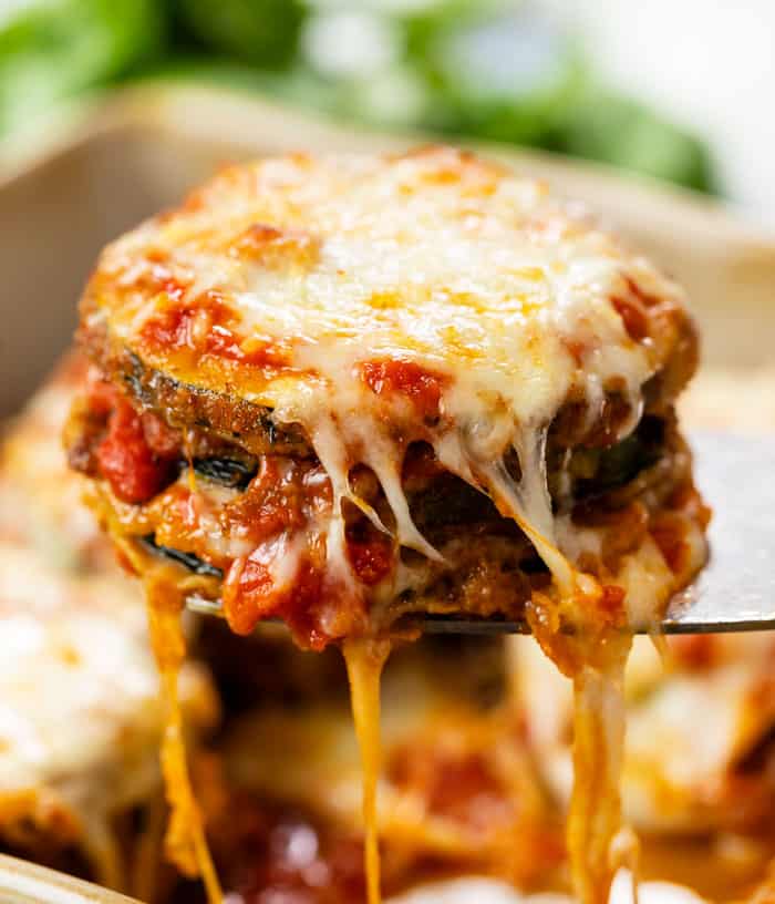 A spatula pulling up cheese zucchini parmesan from a casserole dish.