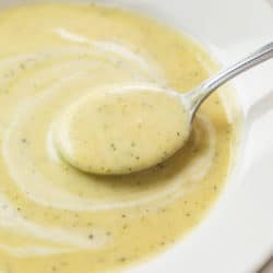 A white soup bowl with a spoon scooping up creamy zucchini soup.