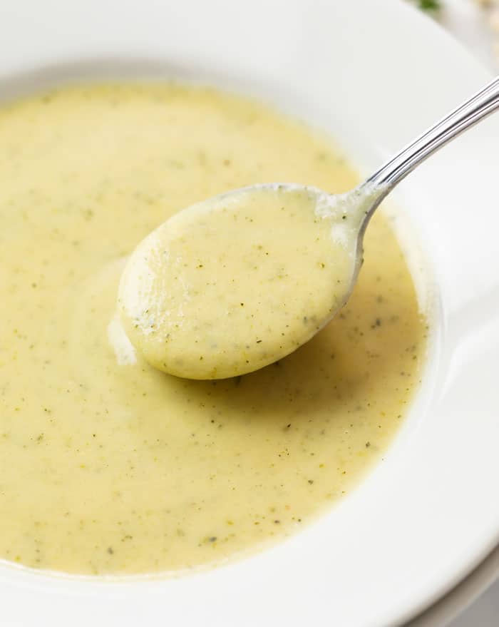 A white bowl with a spoon scooping up zucchini soup.