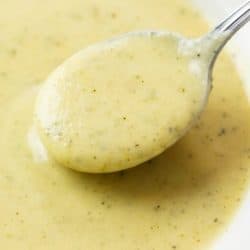 A pin image with a bowl of zucchini soup with a spoon in it.