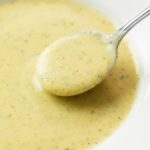 A spoon scooping up creamy Zucchini Soup from a white bowl.