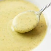 A spoon scooping up creamy Zucchini Soup from a white bowl.