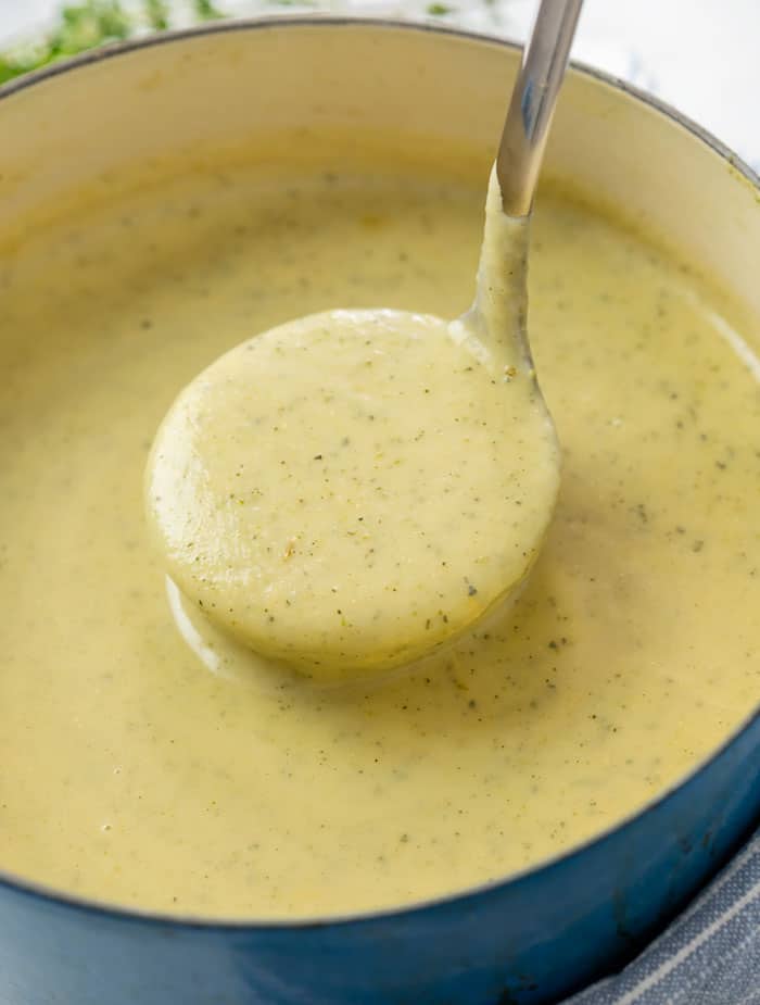 A soup pot filled with a ladle scooping up creamy zucchini soup.