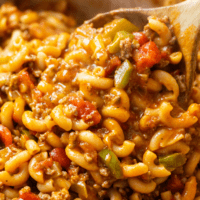 A wooden spoon scooping up American Chop Suey with ground beef, peppers, tomatoes, and sauce.