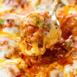 A spoon scooping up a meatball covered in marinara sauce and topped with cheese.