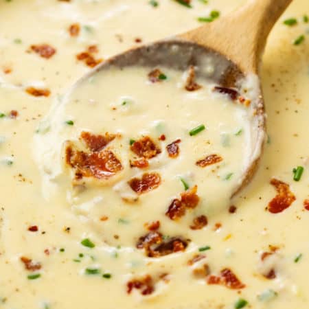 A wooden spoon scooping up baked potato soup topped with bacon and chives.