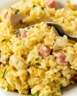 A white plate with a fork scooping up Chicken Cordon Bleu Casserole with ham, chicken, and rice.