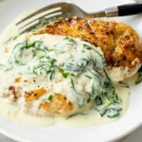 Seared chicken on a white plate topped with creamy Florentine sauce with spinach.
