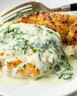 Seared chicken on a white plate topped with creamy Florentine sauce with spinach.