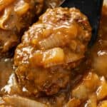 A spatula holding Hamburger Steak smothered in brown gravy with onions.