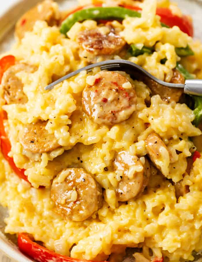 A pile of creamy rice with slices of sausage and peppers with a fork.