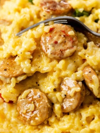 Cheesy rice with slices of cooked sausage and a fork in the background.
