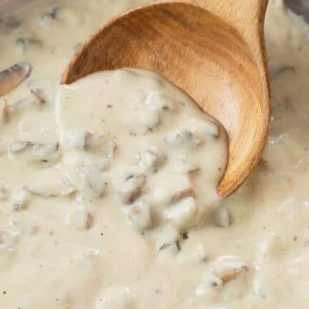 A wooden spoon scooping condensed cream of mushroom soup up from a pan.